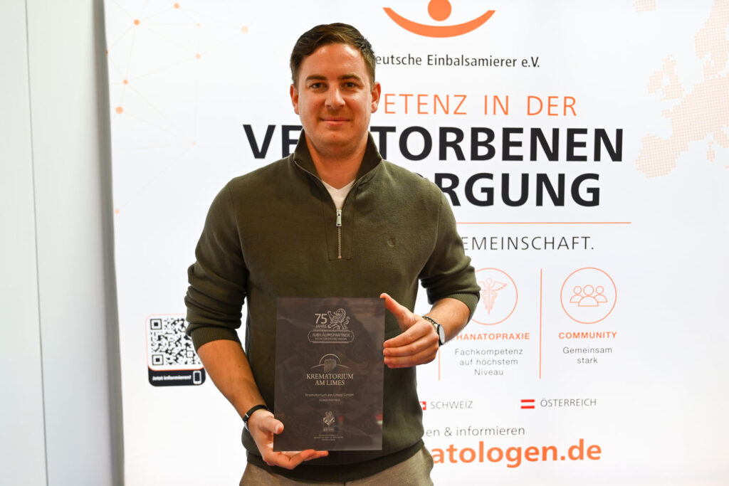 Ein Mitarbeiter des Krematoriums am Limes präsentiert stolz den Jubiläumsaward des Bestatterverbandes Bayern auf der Befa in Düsseldorf. Die Auszeichnungstafel zeigt die Aufschrift „75 Jahre – Jubiläumspartner Bestatterverband Bayern – Krematorium am Limes".