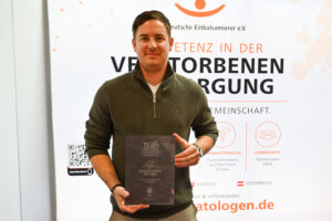 Ein Mitarbeiter des Krematoriums am Limes präsentiert stolz den Jubiläumsaward des Bestatterverbandes Bayern auf der Befa in Düsseldorf. Die Auszeichnungstafel zeigt die Aufschrift „75 Jahre – Jubiläumspartner Bestatterverband Bayern – Krematorium am Limes".